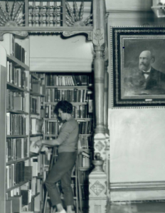 black and white image of a woman shelving library books in the old library inside the Cook Home