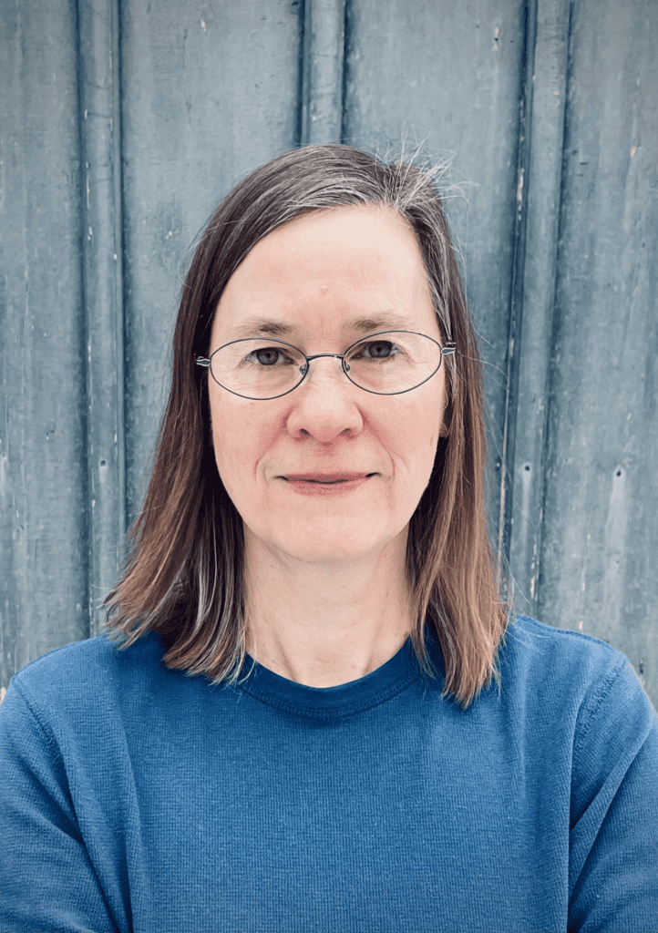 Image of author Sierra Greer, a white woman with oval glasses wearing a blue shirt