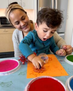 A caregiver and child play with stamps on a table at the Library.