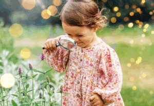 child looking through a magnifying glass at flowers.