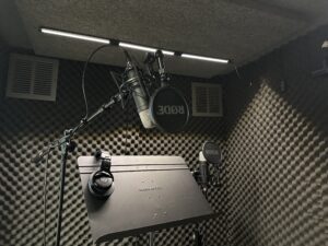 Picture of vocal recording booth with two microphones and a pair of headphones on a music stand. 