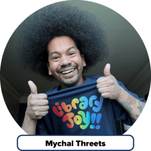 Librarian Mychal Threets smiling with thumbs up gesture while wearing a t-shirt that reads “Library Joy!!”