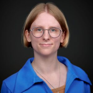 An author photo of Johanna Van Veen: a white woman with short cropped blonde hair and glasses smiles at the camera